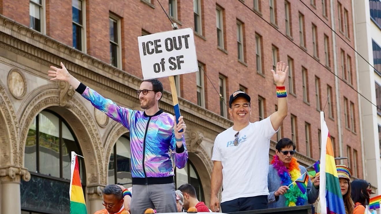 Two people holding signs with 'ICE OUT of SF' at a Pride parade.